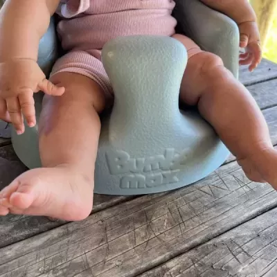 Assento de bebé cinzento com criança vestida de rosa em superfície de madeira