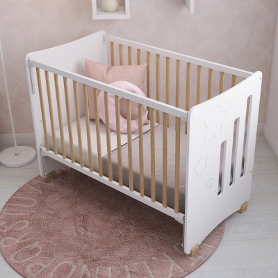 Berço de bebé em madeira com laterais em varas de madeira clara sobre tapete rosa.
