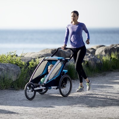 Mulher a correr com um carrinho de corrida azul para bebé à beira-mar