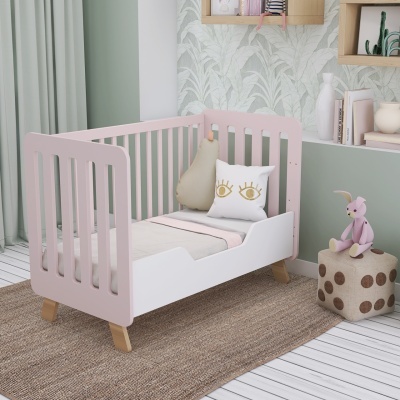 Cama infantil rosa e branca com almofadas e brinquedo num quarto decorado com parede verde e papel de parede de folhas.