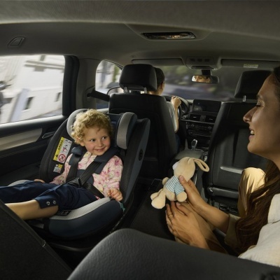Criança num assento auto infantil dentro de carro com mulher a segurar peluche