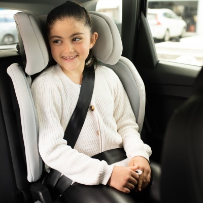 Menina sentada em cadeira auto cinza com cintos pretos dentro de carro.