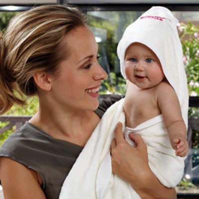 Bebé enrolado em toalha de banho branca com capuz, segurado por mulher