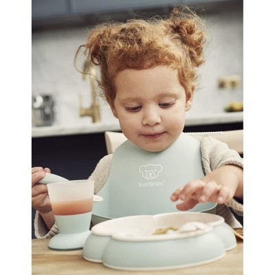 Copo e prato de alimentação e babete verde claro para bebé usados por criança à mesa