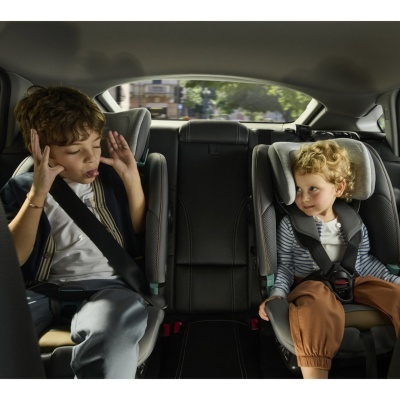 Duas crianças em cadeiras auto cinzentas no banco traseiro de um carro com estofos pretos.