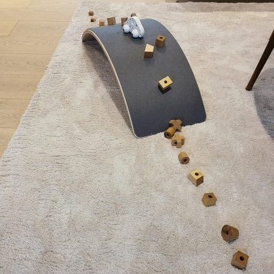 Prancha de equilíbrio em madeira clara com blocos de madeira e brinquedo branco sobre carpete bege