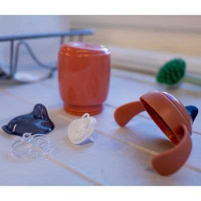 acessórios de bebé incluindo chupetas e peça de silicone castanha numa superfície branca