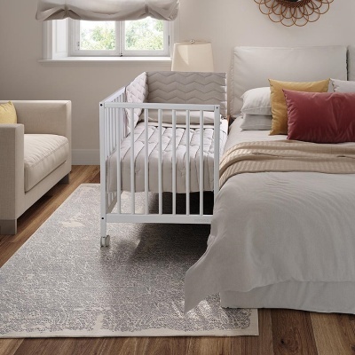 Berço branco com colchão cinza em quarto junto a cama e sofá