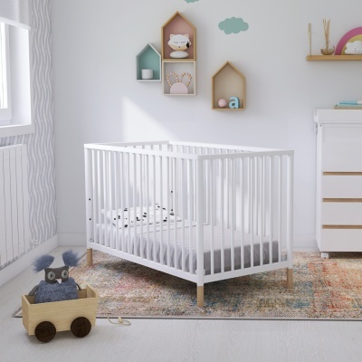 Berço branco de madeira com colchão e almofada, tapete colorido, brinquedo de pelúcia em carrinho de madeira, quarto de bebé com decoração mural