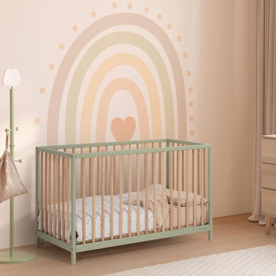 Berço de bebé com estrutura verde pastel e grades de madeira clara num quarto com parede decorada com arco-íris pastel e cabide verde