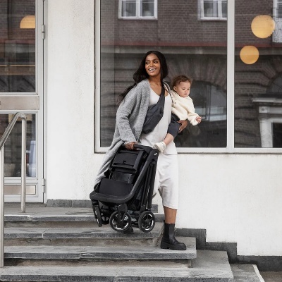 Mulher a descer escadas a carregar um carrinho de bebé dobrado e um bebé ao colo