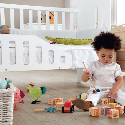 Criança a brincar com blocos de madeira junto a berço branco e almofada verde em forma de crocodilo