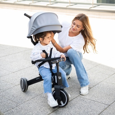 Triciclo preto com capota cinzenta em pavimento cinzento com criança e mulher