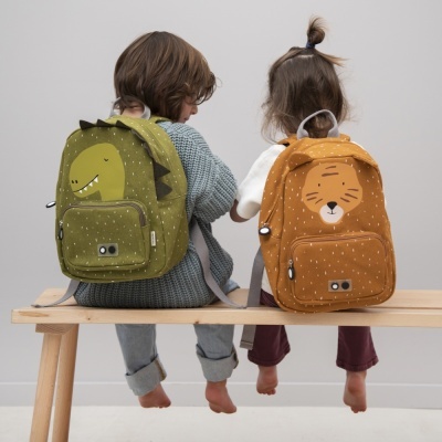 Crianças com mochilas infantis verde de dinossauro e laranja de tigre sentadas num banco de madeira