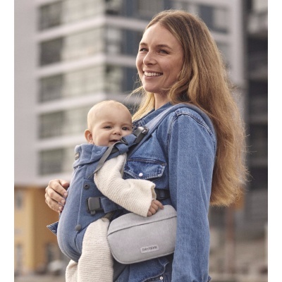Mulher com porta-bebés cinzento e bebê vestido de branco em ambiente urbano