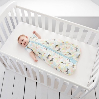 Bebé deitado num saco de dormir estampado dentro de berço branco com colchão branco.