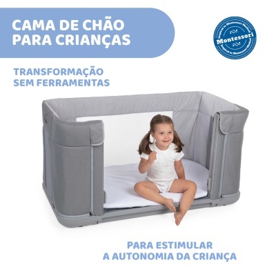 Cama de chão para crianças cinzenta com criança sentada dentro em fundo branco.