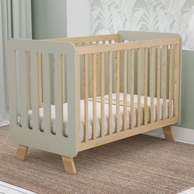 Berço de bebé verde claro e madeira clara num quarto com papel de parede floral