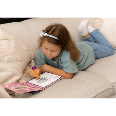 Menina a colorir um livro de pintar num sofá creme.