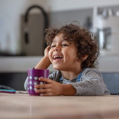 Copo plástico roxo com bolinhas brancas na mão de criança na cozinha