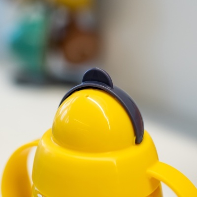 Garrafa amarela com tampa arredondada e alça preta em superfície branca.