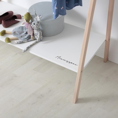 Prateleira branca com pernas de madeira clara, duas bonecas de pano e caixa redonda às riscas