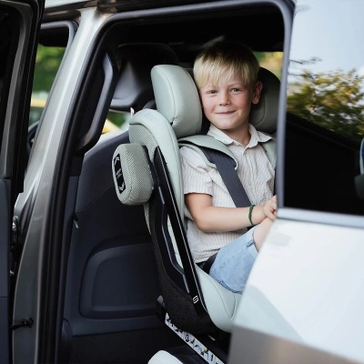 Criança sentada em cadeira auto cinzento claro e preto no banco de trás de carro branco