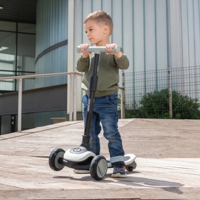 Criança a andar numa trotinete branca e preta com três rodas em superfície de madeira