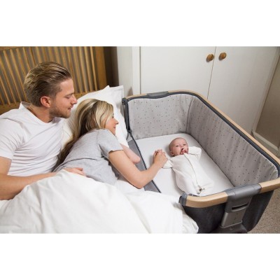 Berço cinzento com padrão de estrelas ao lado da cama com bebé e casal