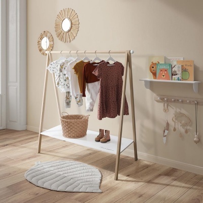 Roupeiro infantil em madeira com roupas, cesto, botas, tapete branco e decoração de parede