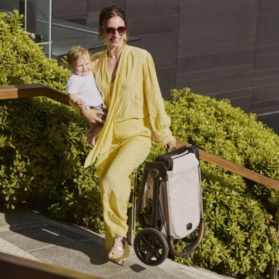 Mulher com fato amarelo e menino seguram carrinho dobrável bege com estrutura metálica