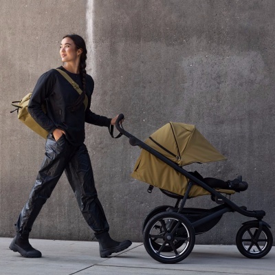 Mulher a puxar carrinho de bebé verde oliva com calças pretas e mochila