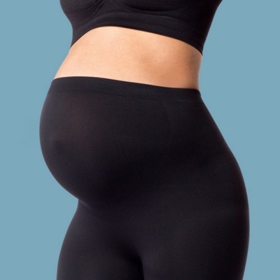 Mulher grávida de perfil com leggings e camisola preta contra fundo azul claro