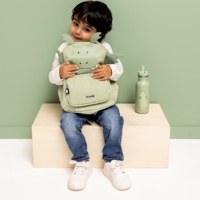 Criança segurando mochila verde de dragão e garrafa verde ao lado