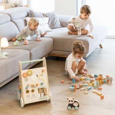 Crianças a brincar com brinquedos de madeira e blocos coloridos numa sala clara com sofá cinza