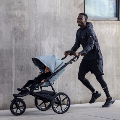 Carrinho de bebé cinzento com rodas pretas e homem a empurrá-lo em ambiente urbano