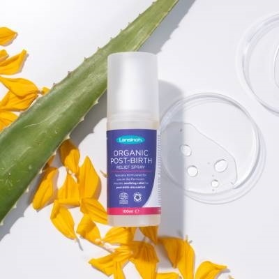 Frasco de spray Lansinoh sobre fundo branco com pétalas amarelas e folha verde