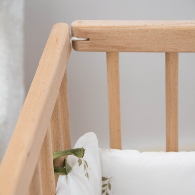 Berço de madeira clara com almofada branca e padrão de folhas verdes