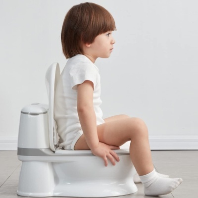 Criança sentada num penico infantil branco com detalhes cinza