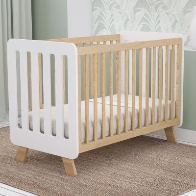 Berço de bebé em madeira e branco com colchão branco numa divisão com tapete e paredes verdes