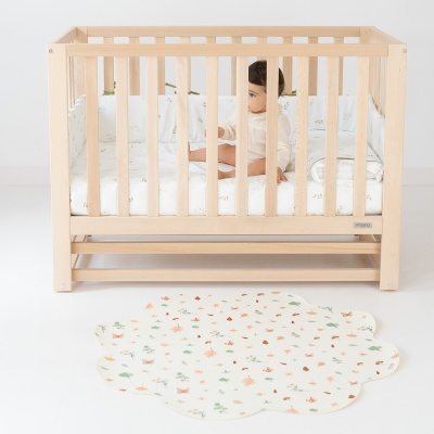Berço de madeira clara com criança dentro e tapete colorido no chão