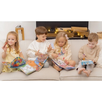 Crianças sentadas num sofá com livros de atividades e marcadores numa sala acolhedora