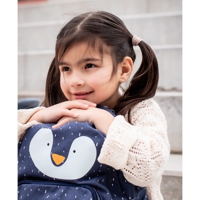 Criança com mochila azul escura de pinguim abraçada sentada em escadas