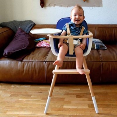 Cadeira alta para bebé em madeira clara e azul com bandeja branca, em chão de madeira em frente a sofá castanho