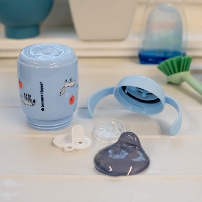 Frasco azul claro com desenhos de animais e acessórios sobre uma superfície branca