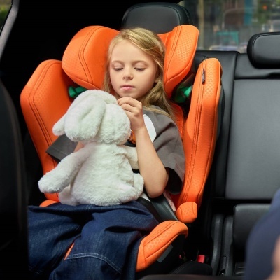 Criança num assento elevatório laranja a segurar um urso de peluche branco dentro de carro preto