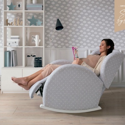 Mulher sentada numa poltrona reclinável cinzenta com padrão de pontos brancos num quarto decorado com papel de parede de estrelas brancas