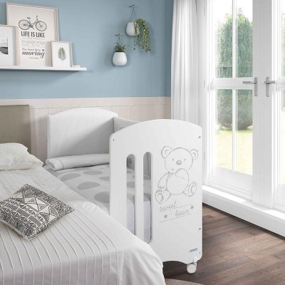 Berço branco com desenho de ursinho e texto 'sweet bear' junto a cama em quarto com parede azul clara