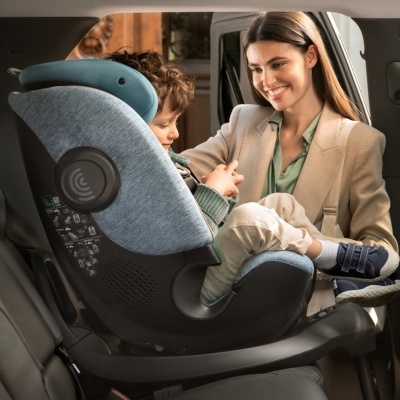 Cadeira auto para criança cinzenta e azul com criança sentado e mulher sorridente ao lado dentro do carro