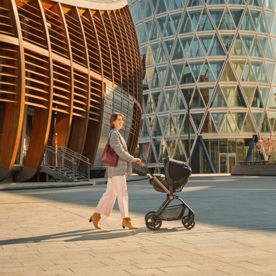 Mulher a empurrar carrinho de bebé preto em espaço urbano com edifícios modernos